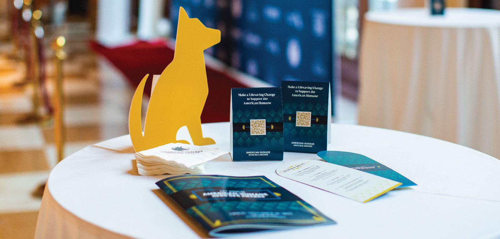 A table with table tents with QR codes, a cut-out dog sign, a program, menus, and branded napkins